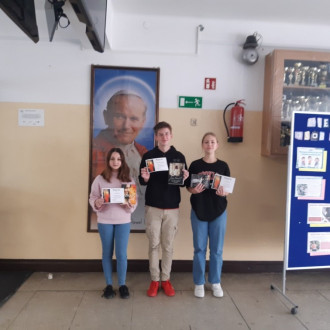 Troje uśmiechniętych uczniów prezentuje dyplomy i nagrody książkowe.