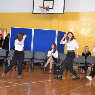 Uczennice klasy ósmej podczas występu tanecznego, w tle  nauczyciel wspomagajacy