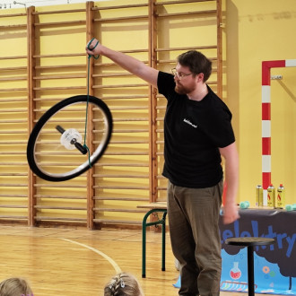 prowadzący pokazuje doświadczenie z kołem rowerowym